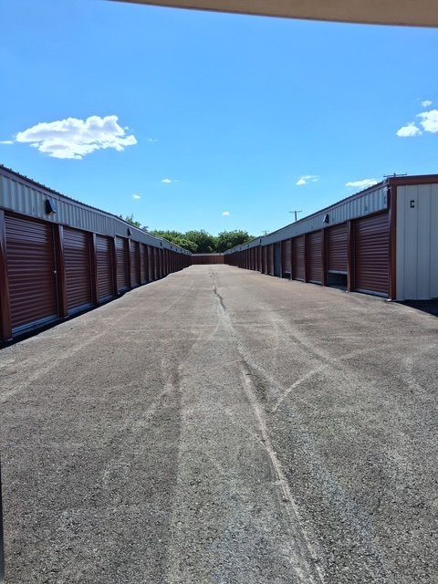 A wide paved drive-up aisle running between two rows of red-door storage units.