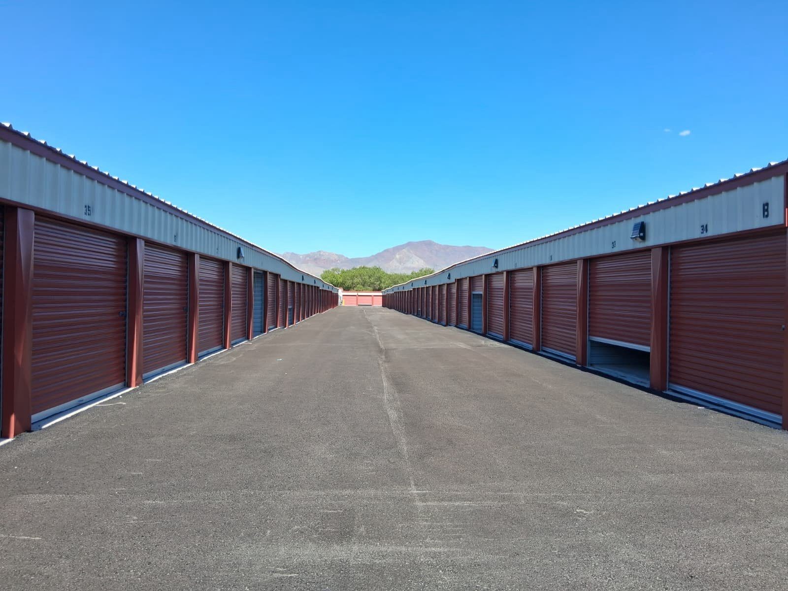 A long symmetrical drive aisle between two rows of storage units with mountain views in the distance at Canutillo Self Storage.