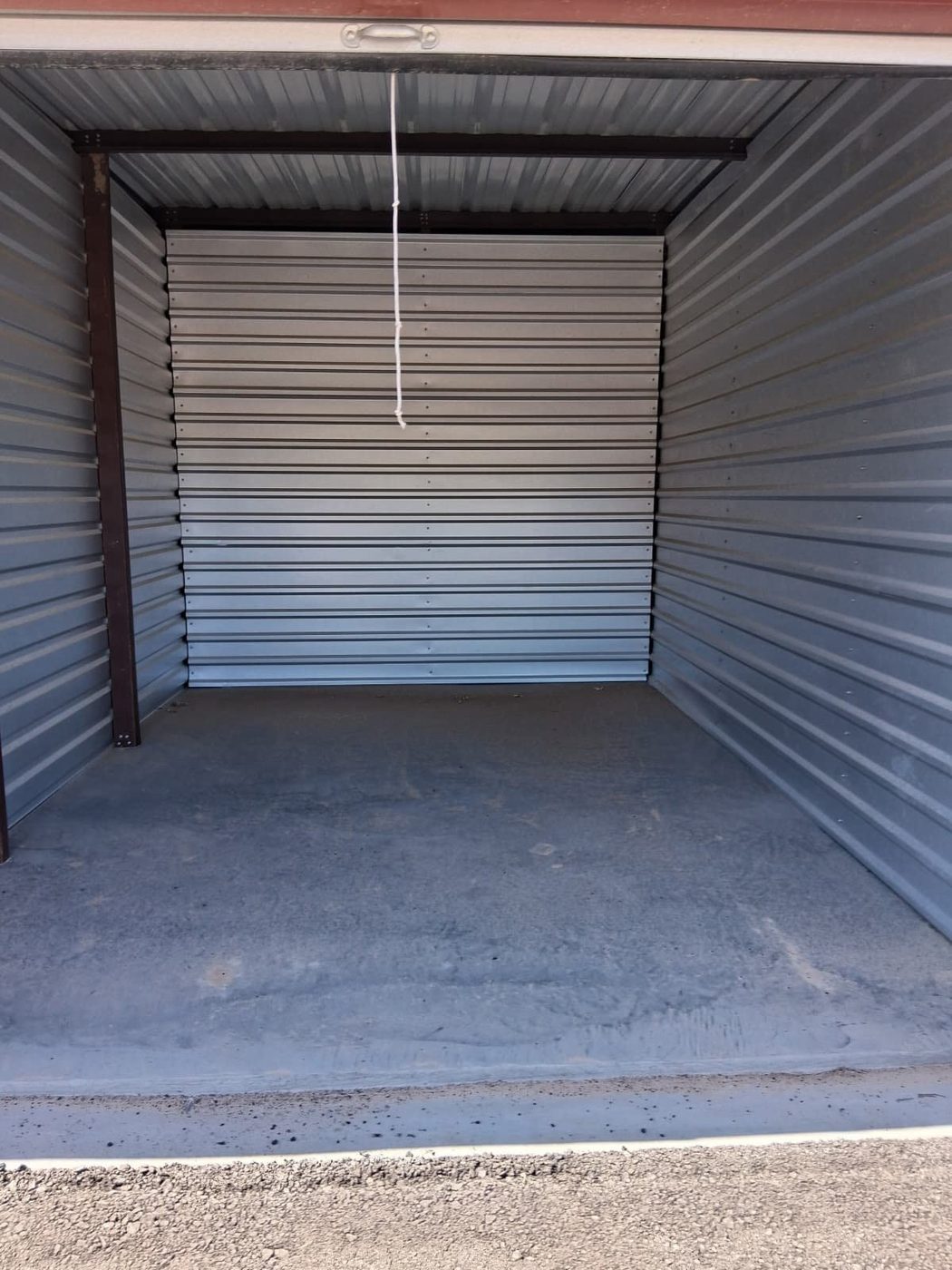 The clean, swept interior of an empty drive-up storage unit with a roll-up door at Canutillo Self Storage.