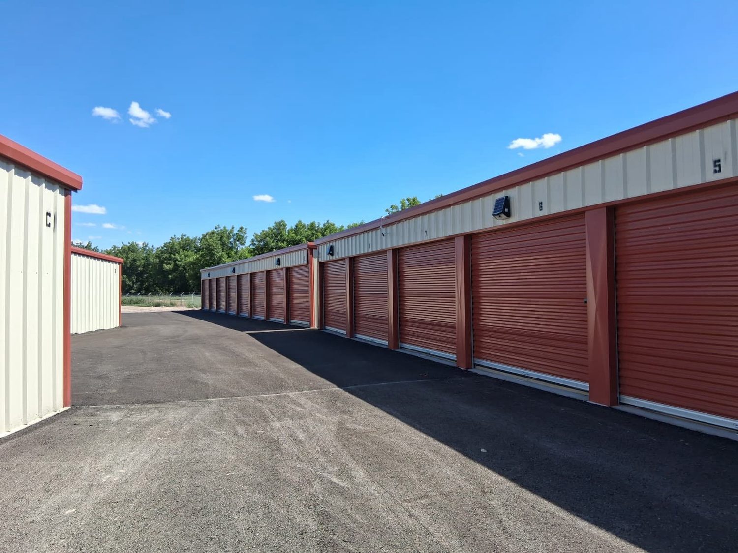 A long, clean row of drive-up storage units with red roll-up doors under a clear blue sky at Canutillo Self Storage.