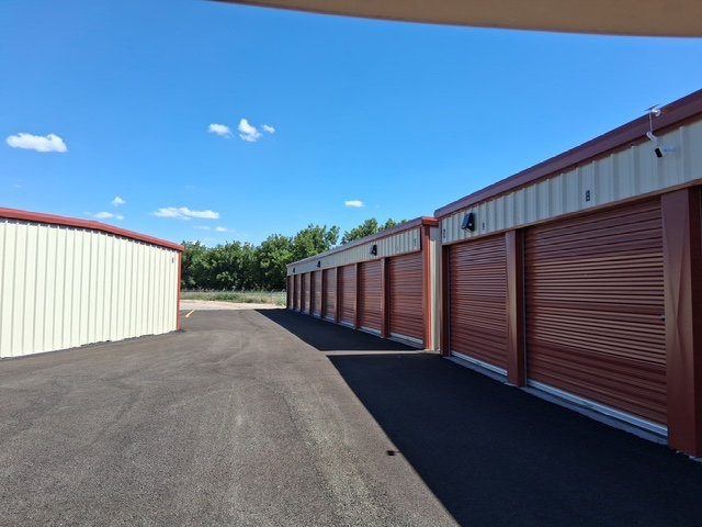 Rows of drive-up storage units with red roll-up doors lining a freshly paved drive at Canutillo Self Storage.
